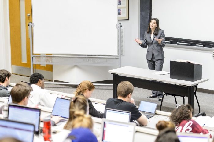 Photo of a professor leaning in to chat with a group of adult students in business attire.