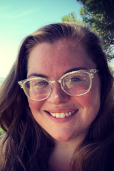 A close-up headshot photo of Charlotte Whatley who has long sandy brown hair and is smiling while wearing light framed round glasses with large lenses