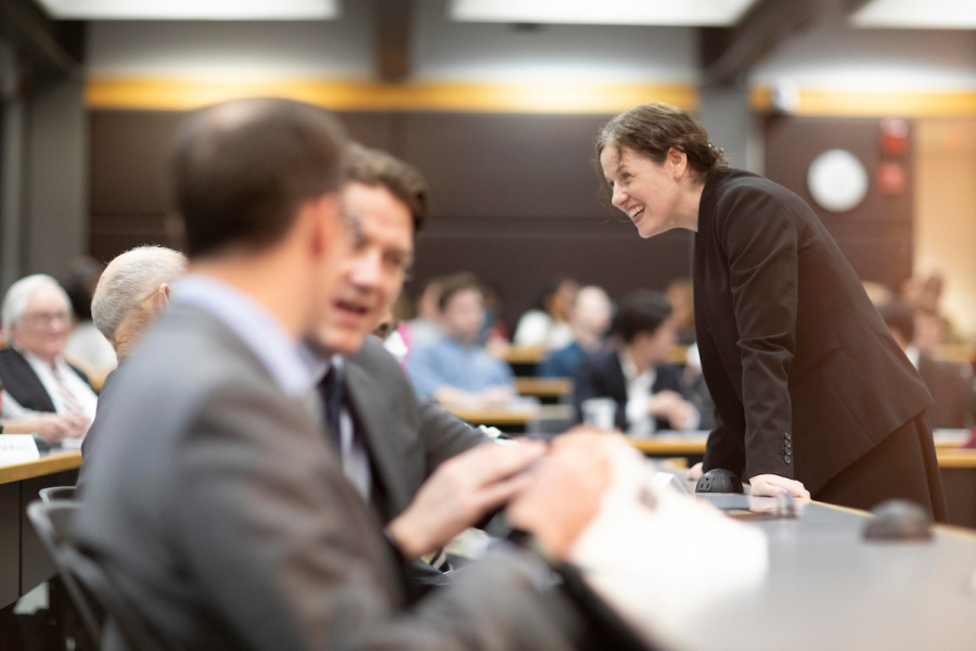 Photo of a professor leaning in to chat with a group of adult students in business attire.