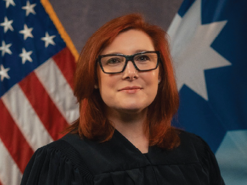 Official photo of Jessica Palmer-Denig smiling in front of the American flag.