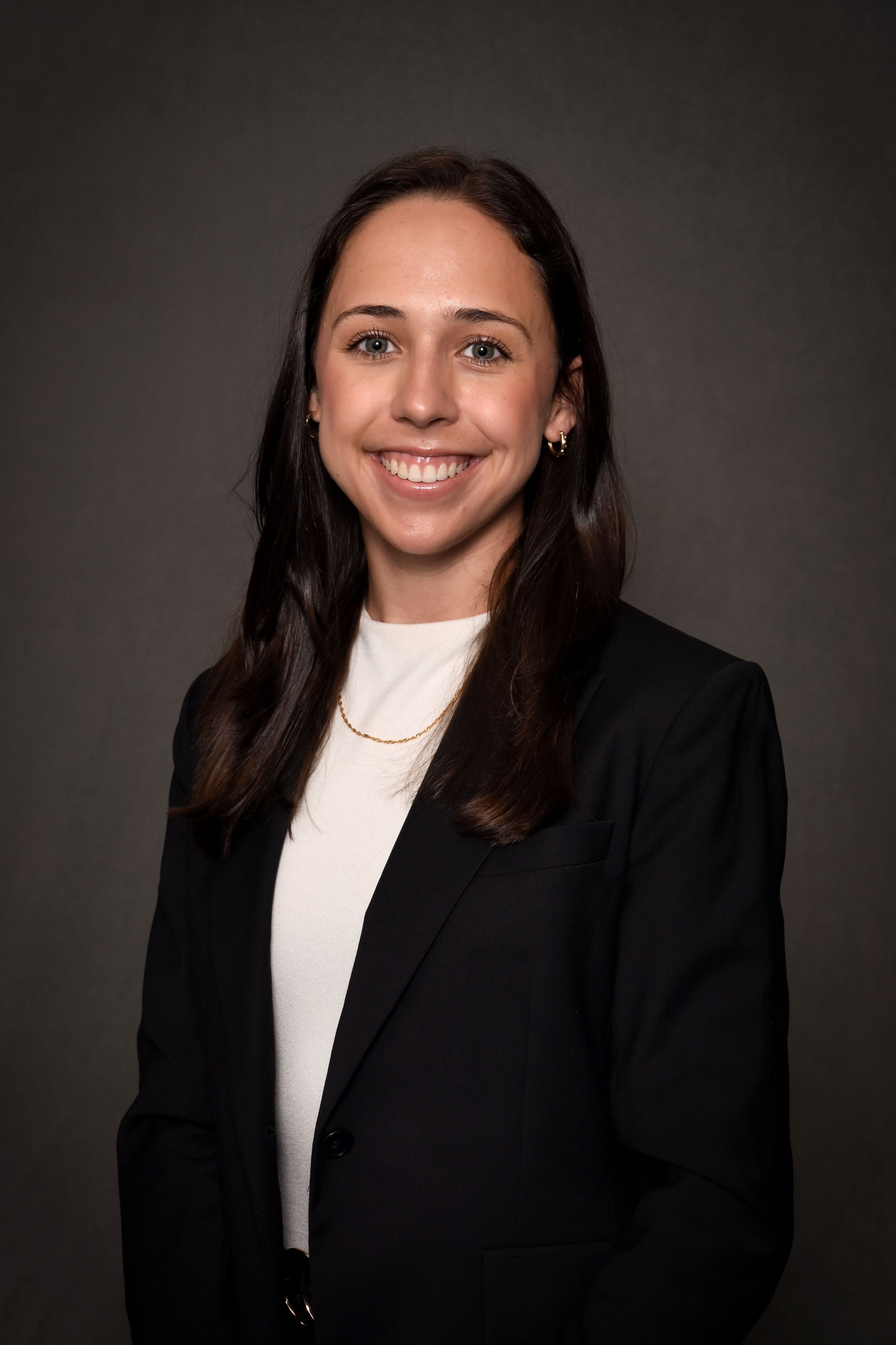 Women in white shirt with black blazer who has long dark brown hair.