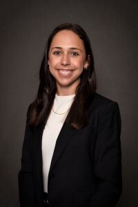 Women in white shirt with black blazer who has long dark brown hair.