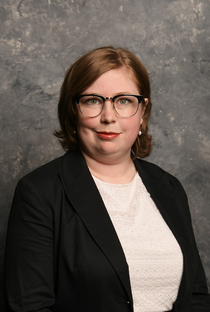 Headshot photo of Amber Sherwood with light skin, glasses, blonde hair, wearing a black blazer with a white top.