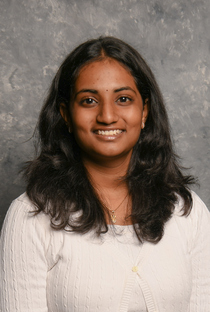 A headshot photo of Nikhita Singam smiling at the camera while wearing a white top with buttons.