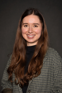 Student with dark brown hair, pin strip blazer and a black shirt