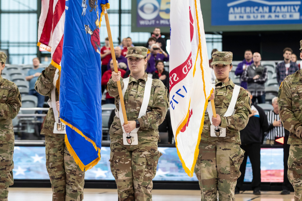 Veterans in camouflage uniforms hold flags at a ceremony.