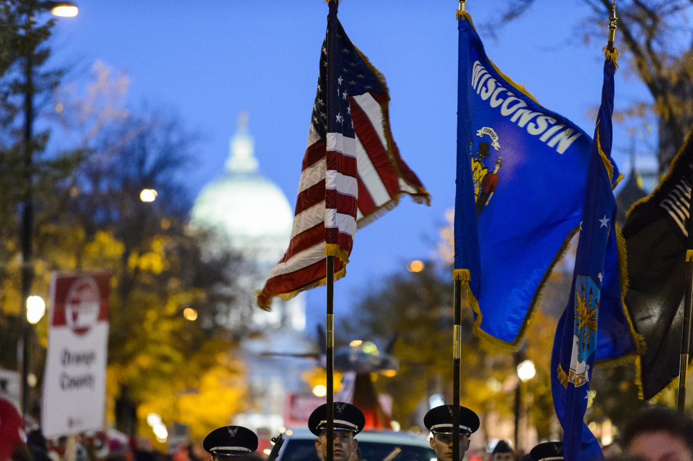 The Wisconsin state flag and American flag standing before a city skyline with the Madison city capitol building in the background.